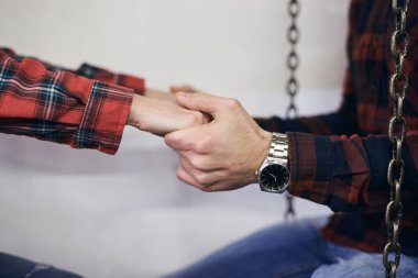 Erkek ve kadın elleri, kırmızı kareli kolları ve kol saati ile birbirlerini tutuyorlar. Romantik Sevgililer Günü kutlaması. El ele tutuşan çiftlerin yakın çekimleri..