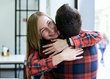 Sarışın, güzel bir kadın, esmer adama sarılıyor, sırtı kameraya dönük. Romantik bir çift, kırmızı kareli gömlekler giyiyorlar, bir kahve dükkanının penceresinde oturuyorlar. Gülümsüyor. Romantik Sevgililer Günü.