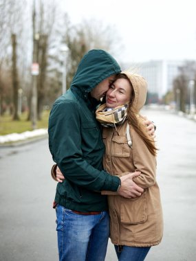 Birbirine aşık genç bir çift, parkta duruyorlar, başlık takıyorlar, sarılıyorlar, yağmurlu bahar gününde birbirlerine bakıyorlar. Romantik Sevgililer Günü Kutlaması