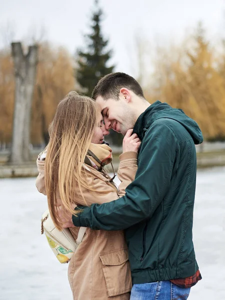 年轻夫妇恋爱了 穿着米黄色和绿色休闲装 站在结冰的湖畔拥抱 在冬天亲吻对方 情人节外面浪漫的庆祝活动 — 图库照片