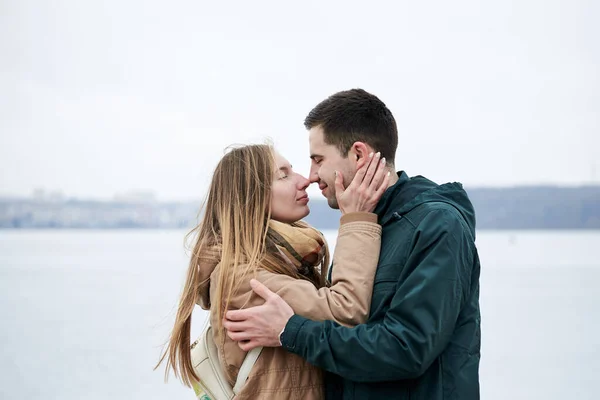 年轻夫妇恋爱了 穿着米黄色和绿色休闲装 站在结冰的湖畔拥抱 在冬天亲吻对方 情人节外面浪漫的庆祝活动 — 图库照片
