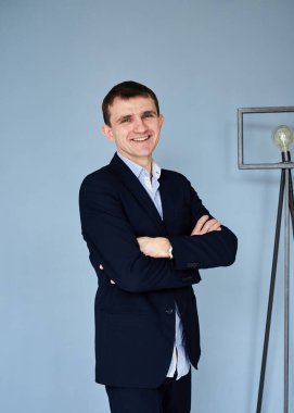 Koyu mavi takım elbiseli, açık mavi gömlekli, mavi duvarın önünde göğsünde çapraz kollar ve sinema lambası olan genç esmer adam, gülümsüyor. Filmin devamı için iş adamı. Şirket kültürü.