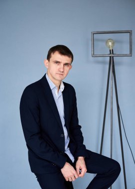 Koyu mavi takım elbiseli, açık mavi gömlekli genç esmer adam, mavi duvarın önünde sinema lambasıyla oturuyor. İş adamı, özgeçmiş için poz veriyor. Şirket kültürü. Duyguların yansıması.