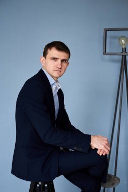 Koyu mavi takım elbiseli, açık mavi gömlekli genç esmer adam, mavi duvarın önünde sinema lambasıyla oturuyor. İş adamı, özgeçmiş için poz veriyor. Şirket kültürü. Duyguların yansıması.