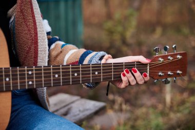 Renkli hırka giyen, akustik gitar çalan, gitar klavyesinin yakından çekilmiş resmi hippi müzisyenlerin bilezikleriyle el ele tutuşan genç bir kadın. Gitar çalmak.