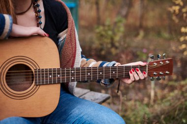 Renkli hırka giyen, akustik gitar çalan, gitar klavyesinin yakından çekilmiş resmi hippi müzisyenlerin bilezikleriyle el ele tutuşan genç bir kadın. Gitar çalmak.