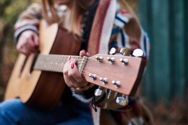 Renkli hırka giyen, akustik gitar çalan, gitar klavyesinin yakından çekilmiş resmi hippi müzisyenlerin bilezikleriyle el ele tutuşan genç bir kadın. Gitar çalmak.