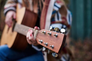 Renkli hırka giyen, akustik gitar çalan, gitar klavyesinin yakından çekilmiş resmi hippi müzisyenlerin bilezikleriyle el ele tutuşan genç bir kadın. Gitar çalmak.