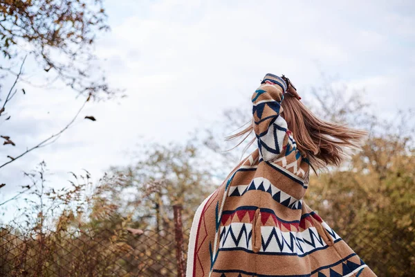 Güz parkı ormanlarında koşan güzel sarışın bir kadının çeyrek portresi. Genç kız, kot pantolon ve renkli hırka giyiyor, doğal arka planda poz veriyor, eğleniyor. Hippi tarzı..
