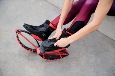 Kangoo atlayışlarının düğmelerini ilikleme sürecindeki ellerin yakın plan fotoğrafı. Genç kadın bacakları, mor tayt giyiyor, kangoo ayakkabıları giyiyor, fitness antrenmanına hazırlanıyor.