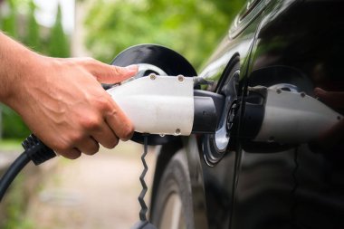 Yeşil ortamda elektrikli arabaya mans el takma şarj cihazı fişi. Yeni enerji aracı, Nev elektrik enerjisi ile yükleniyor. Ekoloji, günümüz arabaları