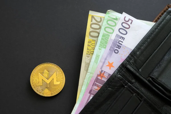 Moneda Monerd junto a billetes de banco en euros que sobresalen de una billetera sobre fondo negro. Moneda digital, mercado de cadena de bloques. Billetes de euros junto a la moneda criptográfica — Foto de Stock