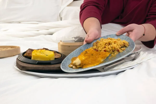 Room service food on the bed in a hotel room. Woman enjoying luxurious room service treat. Lazy morning in bed, eating in bed during holidays