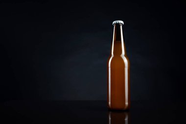Siyah kapaklı soğuk açılmamış bira şişesi. Bir bardak buzlu buğday ya da koyu arkaplanda bira.