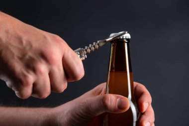 Siyah arka planda kapaklı soğuk bira şişesi açan adamlar. Dondurulmuş buğday kıran eller ya da koyu arkaplanda bir açacağı olan bira.