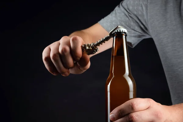 Männer öffnen eine kalte Bierflasche mit Deckel auf schwarzem Hintergrund. Hände knacken gekühltes Weizen- oder Lagerbier mit einem Öffner auf dunklem Hintergrund — Stockfoto