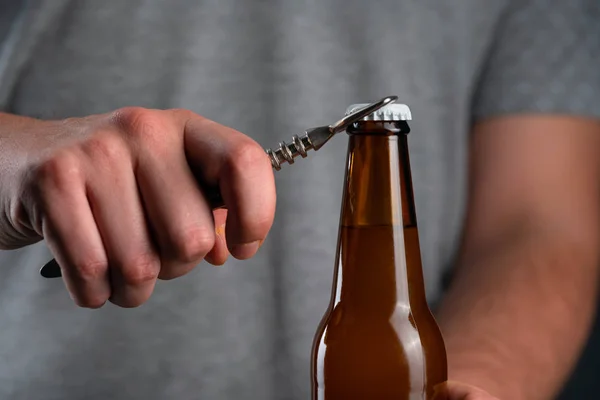 Männer öffnen eine kalte Bierflasche mit Deckel auf schwarzem Hintergrund. Hände knacken gekühltes Weizen- oder Lagerbier mit einem Öffner auf dunklem Hintergrund — Stockfoto