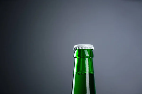 Cold unopened bottle of beer with cap on black background. Glass of refrigerated wheat or lager beer on dark background