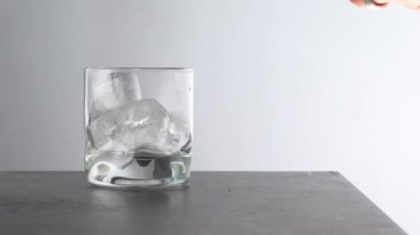 Barmen, masada buz küpleri olan bir bardağa yıllanmış altın viski dolduruyor. Kehribar renkli, beyaz arka planda taşlar olan alkol içeceği.