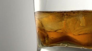 Masasında buz küpleri olan bir bardak yıllanmış altın viski. Kehribar boyalı içki ve bardaki taşlar.