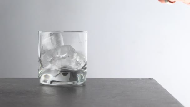 酒吧招待把陈腐的金色威士忌倒入桌上放着冰块的杯子里 琥珀色酒精饮料 有白色背景的岩石 — 图库视频影像