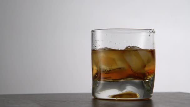 テーブルの上に氷のキューブと高齢者の黄金のウイスキーのガラス バーで岩と琥珀色のアルコール飲料 — ストック動画
