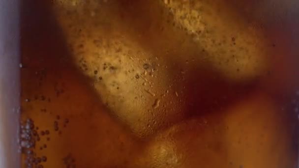 コーラのガラスの中で氷で上昇泡のショットを閉じます カフェイン入りの冷たい飲み物の炭酸飲料のマクロショット — ストック動画