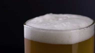 Siyah arka planda beyaz köpüklü taze ve soğuk bira bardağını kapat. Makro köpüklü buğday ya da koyu arkaplanda bira.