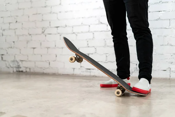 Zblízka skateboardista stojící vedle bílé cihlové zdi. Sportovní teenager v džínách se skateboardem. Městský styl, kultura mládeže — Stock fotografie