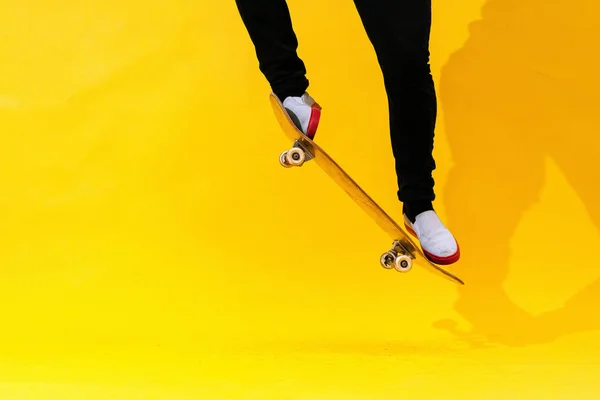 Skateboarder performing skateboard trick - ollie on concrete. Studio shot of olympic athlete practicing jump on yellow background, preparing for competition. Extreme sport, youth culture