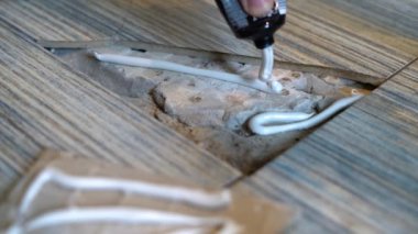 Close up view of man fixing broken tile in the bathroom. Hands renovate cracked asbestos floor tile. Damaged ceramic tile