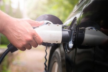 Yeşil ortamda elektrikli arabaya mans el takma şarj cihazı fişi. Yeni enerji aracı, Nev elektrik enerjisi ile yükleniyor. Ekoloji, günümüz arabaları