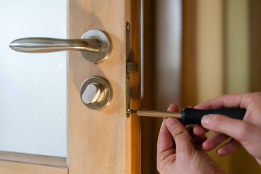 Marangoz kapı kilidini tamir ediyor. Kapı kolu takıyorum. Kapı menteşesini sıkılaştıran tamirci. Tornavidayla tamircinin elleri. Çilingir tahta kapıya vida vidalıyor.