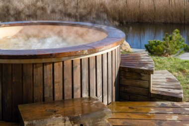 Dışarıdaki ahşap jakuzide su nasıl da kıvrılıyor. Güneşli bir günde sıcak havuzun tadını çıkarmak, özel spa tedavisi. Kimse.
