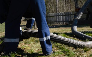 Boru tutan işçi, dışarıdaki kanalizasyon temizleme servisini sağlıyor. Kanalizasyon pompalama makinesi tıkanmış rögar kapağını açıyor