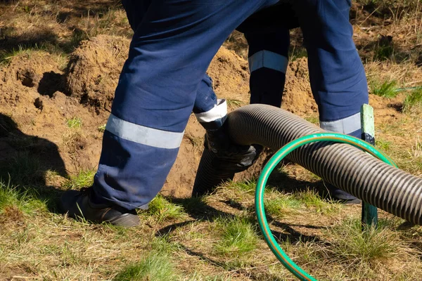 Boru tutan işçi, dışarıdaki kanalizasyon temizleme servisini sağlıyor. Kanalizasyon pompalama makinesi tıkanmış rögar kapağını açıyor