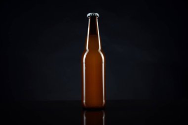 Siyah kapaklı soğuk açılmamış bira şişesi. Bir bardak buzlu buğday ya da koyu arkaplanda bira.