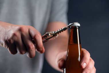 Siyah arka planda kapaklı soğuk bira şişesi açan adamlar. Dondurulmuş buğday kıran eller ya da koyu arkaplanda bir açacağı olan bira.