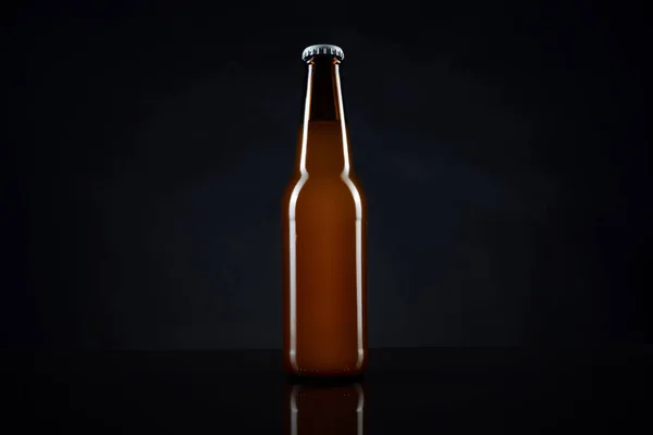 Cold unopened bottle of beer with cap on black background. Glass of refrigerated wheat or lager beer on dark background
