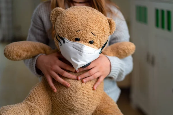 Teenage girl hugging teddy bear with face mask. Concept of corona virus, staying at home, isolation. Preventing flu virus