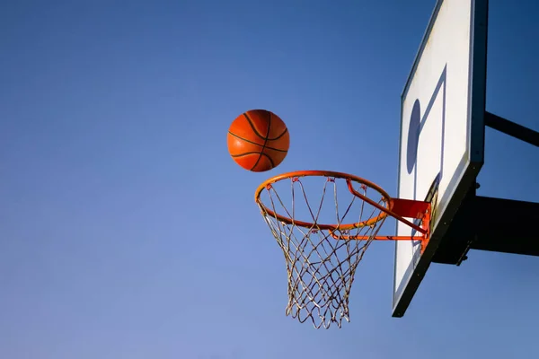Sokak basketbolu potaya düşüyor. Arka planda mavi gökyüzü olan turuncu topu potanın üzerine yaklaştır. Başarı kavramı, sayı yapma ve kazanma. Boşluğu kopyala