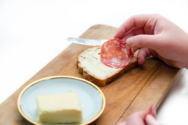 Salam sosisini beyaz ekmeğe, tereyağını da mutfaktaki tahta kesme tahtasına koy.