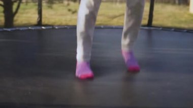 Arka bahçede trambolinde zıplayan küçük bir kız. Trambolinde zıplayan bir genç.