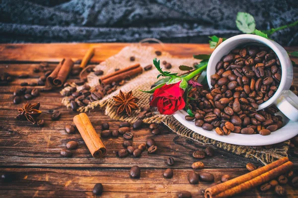 Tazza riempita con chicchi di caffè su vecchio tavolo di legno con rose sullo sfondo . — Foto Stock