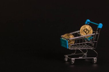 Altın bitcoin paralar siyah bir arka planda süpermarket tramvayında parlar.