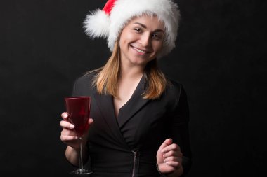 Noel Baba şapkalı kırmızı gözlüklü güzel kız siyah arka planda gülümsüyor..