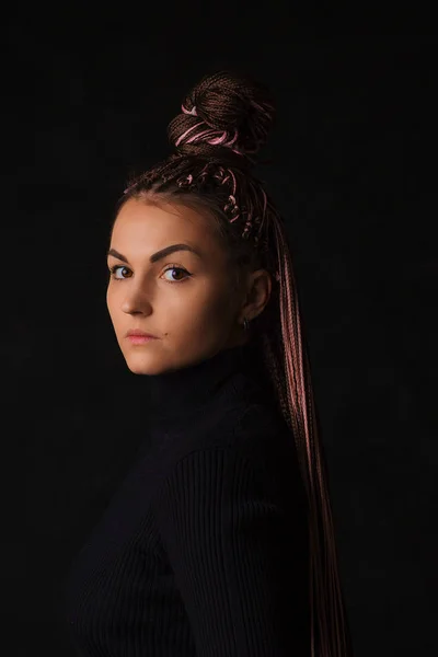 A beautiful girl with pink afro or zizi pigtails and brown eyes looks sternly at the camera on a black background. — 스톡 사진