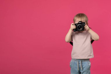 SaINT-PETERSBURG, RUSSİA - 22 Mart 2020: Bir çocuk elinde EF 50mm 1.4 'lük mercekli bir Canon 70d kamera tutuyor ve pembe bir stüdyonun arka planında fotoğraf çekiyor..