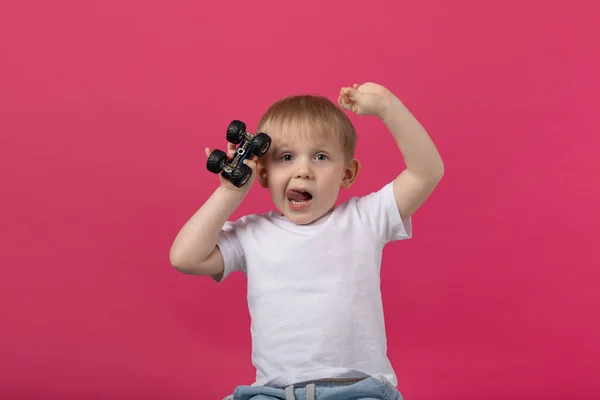 一个男孩手里拿着一台带着轮子的打字机 挥挥手 伸出舌头 看着摄像机 工作室拍摄了一个粉色背景的文章关于好玩的模型 — 图库照片