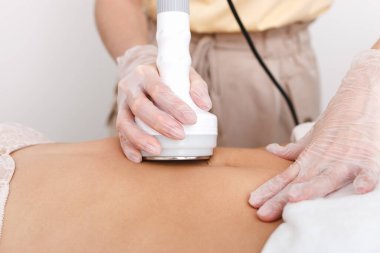 Kozmetik uzmanı modelin karın boşluğunda oyuklaşma, figürün donanım düzeltmesi, aşırı kilonun tahrip edilmesi veya yağ hücreleri yapar. Beyaz bir duvara yakın çekim stüdyosu.